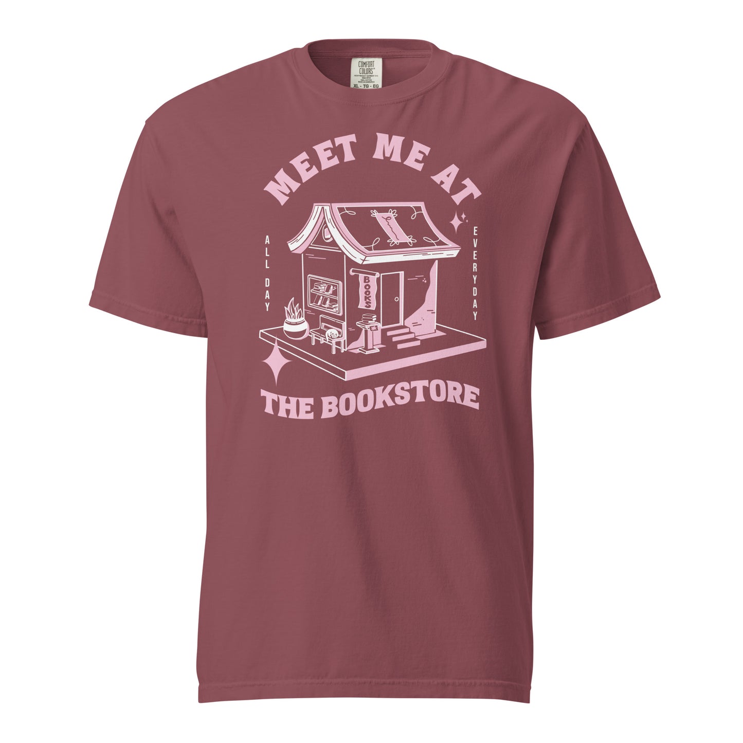Brick Comfort Colors t-shirt with a hand-drawn design of a bookstore with a cute cat on a bench and books in the window, and an open book as a roof, with the text "Meet me at the Bookstore", Vertical text on either side reads all day, and everyday.