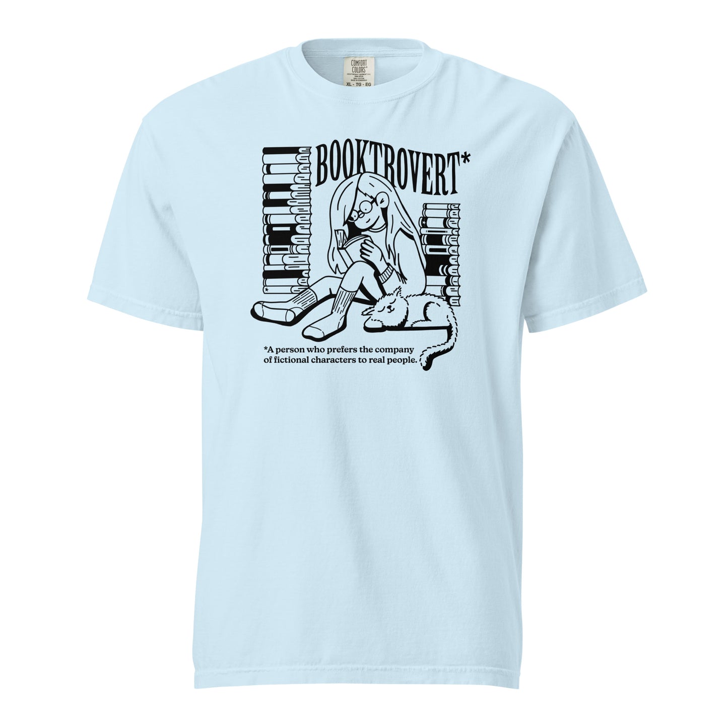 Chambray Blue Comfort Colors t-shirt with the text "Booktrovert." A woman holds a book reading, with her cat sitting next to her sleeping. Behind her are two piles of books. The bottom reads "A person who prefers the company of fictional characters to read people."