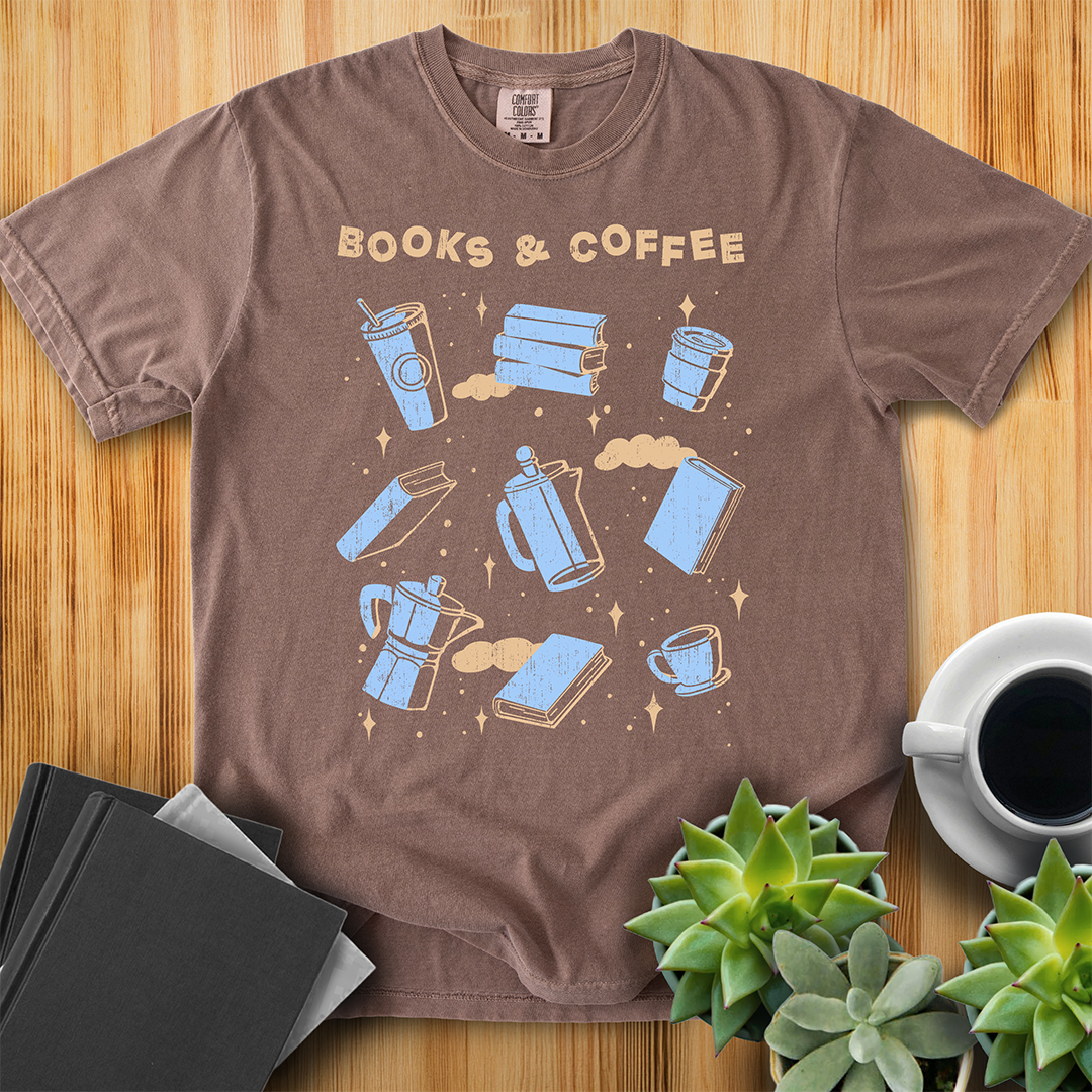 Espresso Brown t-shirt with Books and Coffee Design. It features the text "books and coffee" at the top, and then a grid of 9 hand-drawn illustrations of various books and coffee, finished with some stars and clouds in the background. The shirt sits on a wood floor with plants, coffee, and books placed around it.