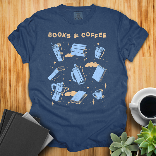Navy Blue t-shirt with Books and Coffee Design. It features the text "books and coffee" at the top, and then a grid of 9 hand-drawn illustrations of various books and coffee, finished with some stars and clouds in the background. The shirt sits on a wood floor with plants, coffee, and books placed around it.