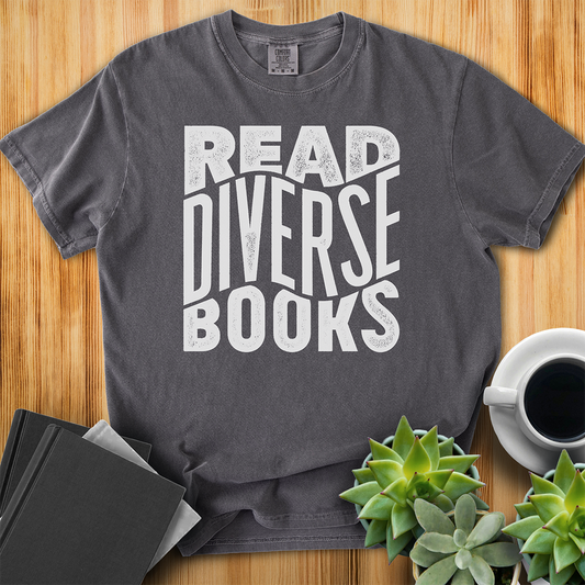 Pepper Gray t-shirt with hand lettered design that says "Read Diverse Books" in white text. The shirt sits on a wood floor with plants, coffee, and books placed around it.