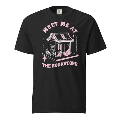 Black Comfort Colors t-shirt with a hand-drawn design of a bookstore with a cute cat on a bench and books in the window, and an open book as a roof, with the text "Meet me at the Bookstore", Vertical text on either side reads all day, and everyday.