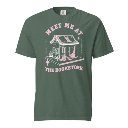 Blue Spruce Comfort Colors t-shirt with a hand-drawn design of a bookstore with a cute cat on a bench and books in the window, and an open book as a roof, with the text "Meet me at the Bookstore", Vertical text on either side reads all day, and everyday.