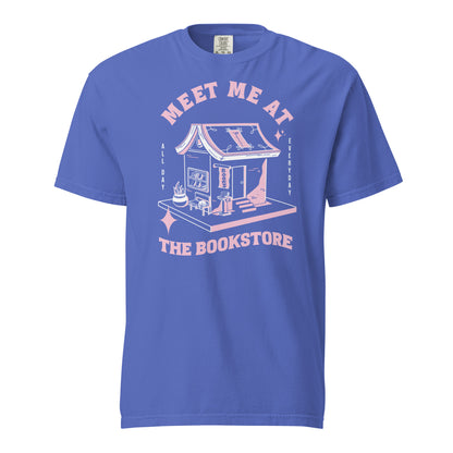Flo Blue Comfort Colors t-shirt with a hand-drawn design of a bookstore with a cute cat on a bench and books in the window, and an open book as a roof, with the text "Meet me at the Bookstore", Vertical text on either side reads all day, and everyday.