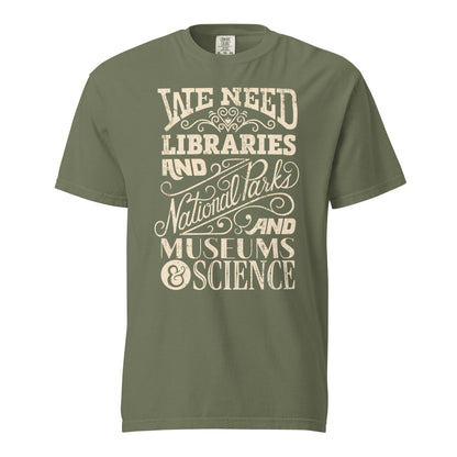 Moss Green Comfort Colors t-shirt with a hand lettered typography design reading "We Need Libraries and National Parks and Museums and Science."