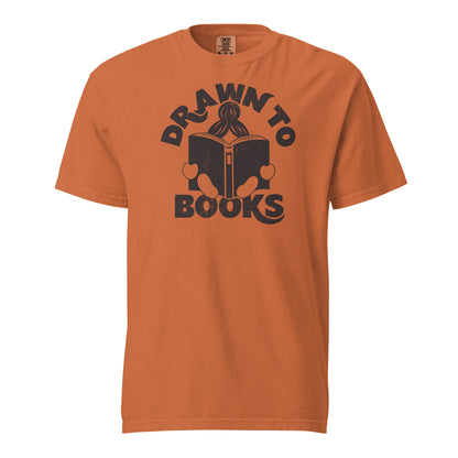 Yam Orange t-shirt with Drawn to Books logo, text says "Drawn to Books" which is framed around a girl reading a book, and you can see only the top of her ponytail, hands and feet, and the big book she's reading.